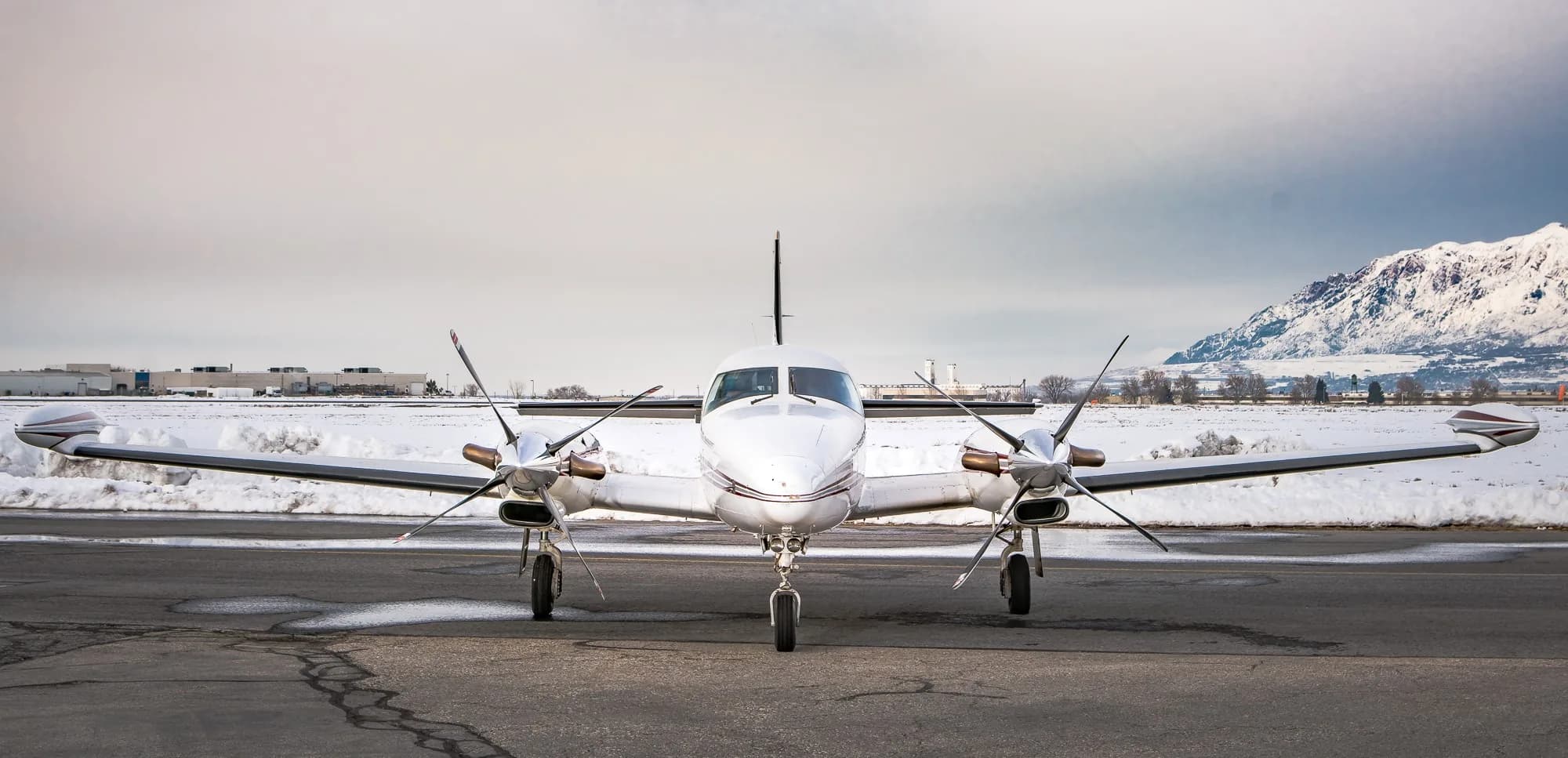 Twin turboprop aircraft parked on a snow covered ramp at sunrise